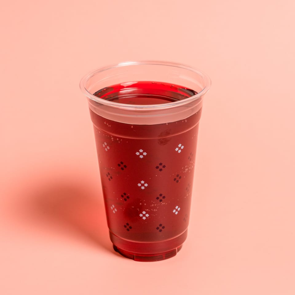 A plastic cup of red Mexican agua fresca with white and black floral patterns.