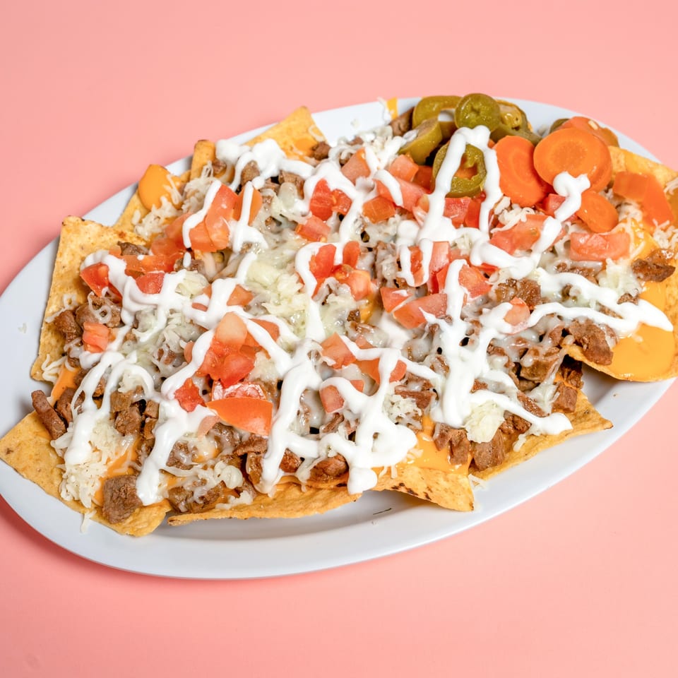 A large plate of nachos with meat, cheese, tomatoes, sour cream, jalapeños, and carrots.
