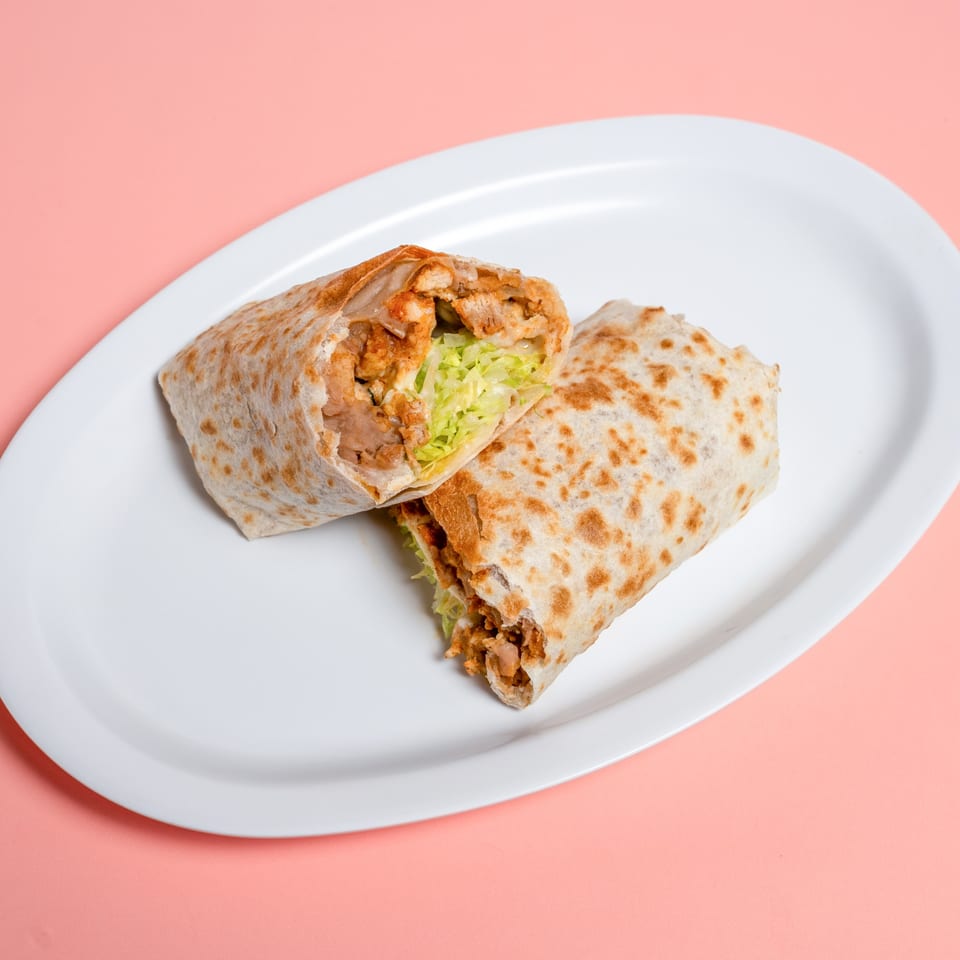 Two halves of a chicken burrito with lettuce on a white oval plate against a pink background.