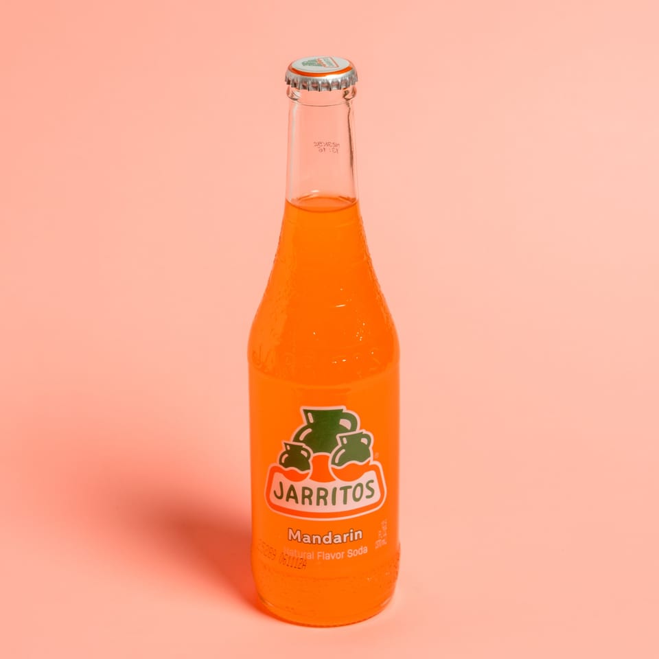 A bottle of Jarritos Mandarin soda with an orange label on a peach background.