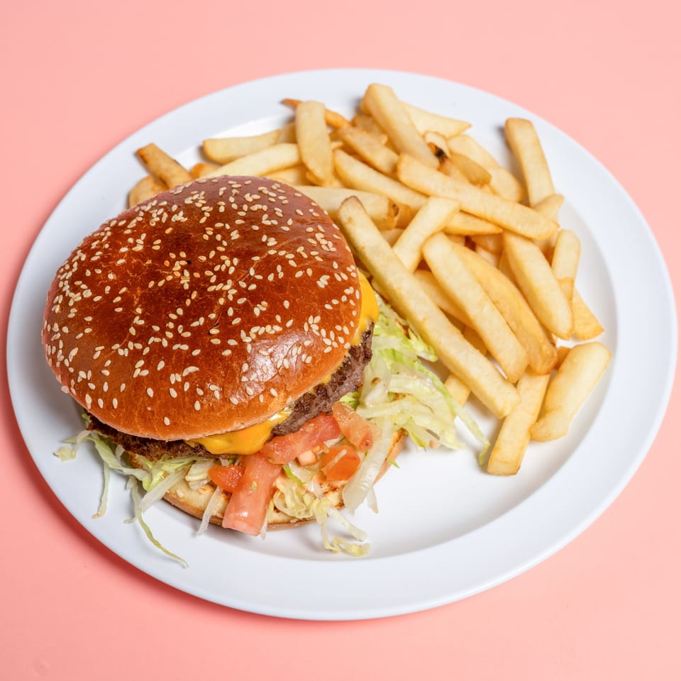 Cheeseburger with lettuce, tomato, and a side of golden french fries on a white plate.