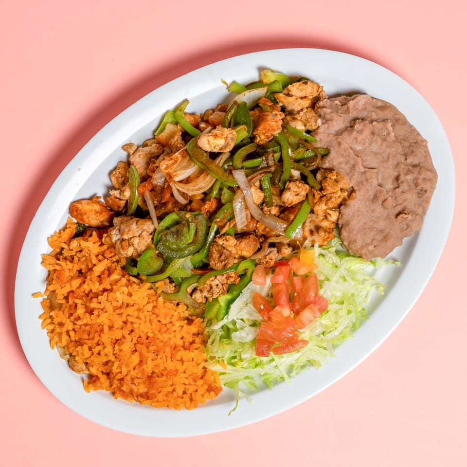 Chicken fajitas with rice, refried beans, lettuce, and diced tomatoes on a white oval plate.